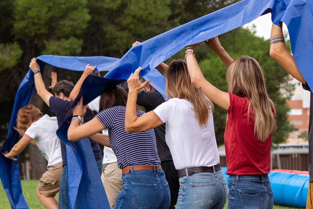 Un equipo hace una dinámica de grupo al aire libre con una lona azul